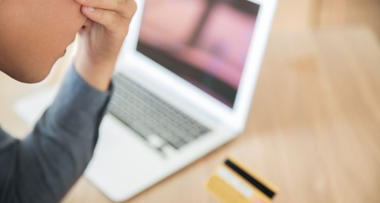 男子拿著信用卡在筆電前懊惱，象徵台灣包養平台詐騙風險與防詐安全意識的重要性。