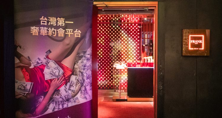 taiwan private party 2026-4 › Sugarbook | The #1 Sugar Daddy & Sugar Baby Dating website to meet Sugar Daddies & Sugar Babies. Build relationships, discuss allowances and get paid instantly. Nightclub entrance with red neon lights inside; a tall advertising banner on the left promoting Sugarbook and Chinese text near a doorway labeled FRANK in a dark exterior setting.
